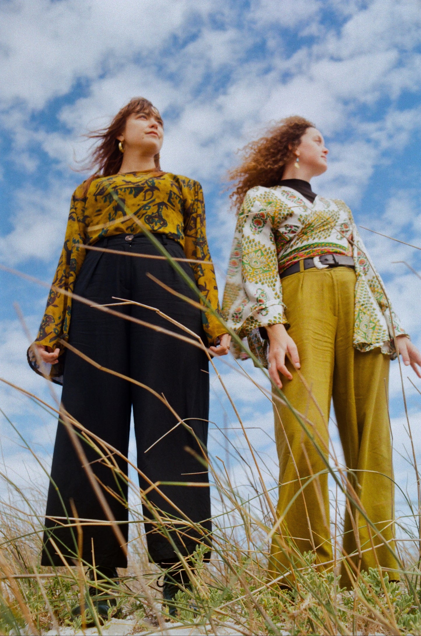 Two women standing in a field with a blue sky and clouds.