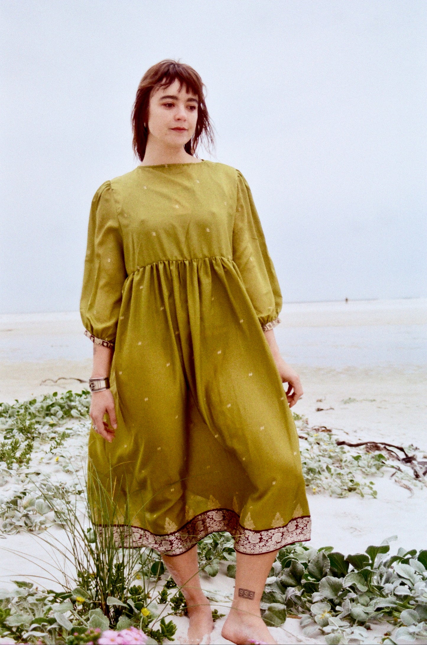 Woman in a green dress standing on a beach with a blurred background