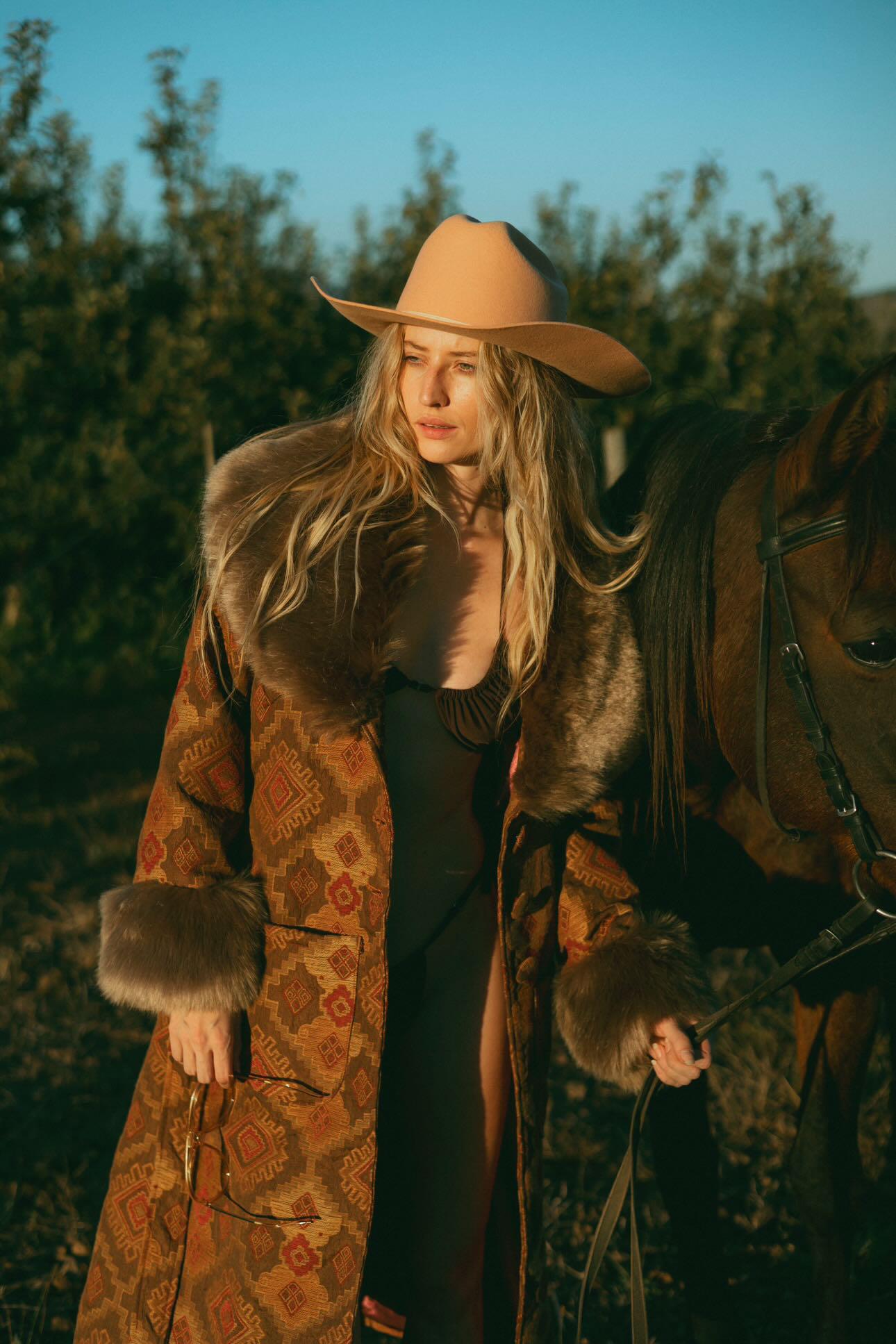 A woman standing next to a horse at sunset wearing a penny lane coat