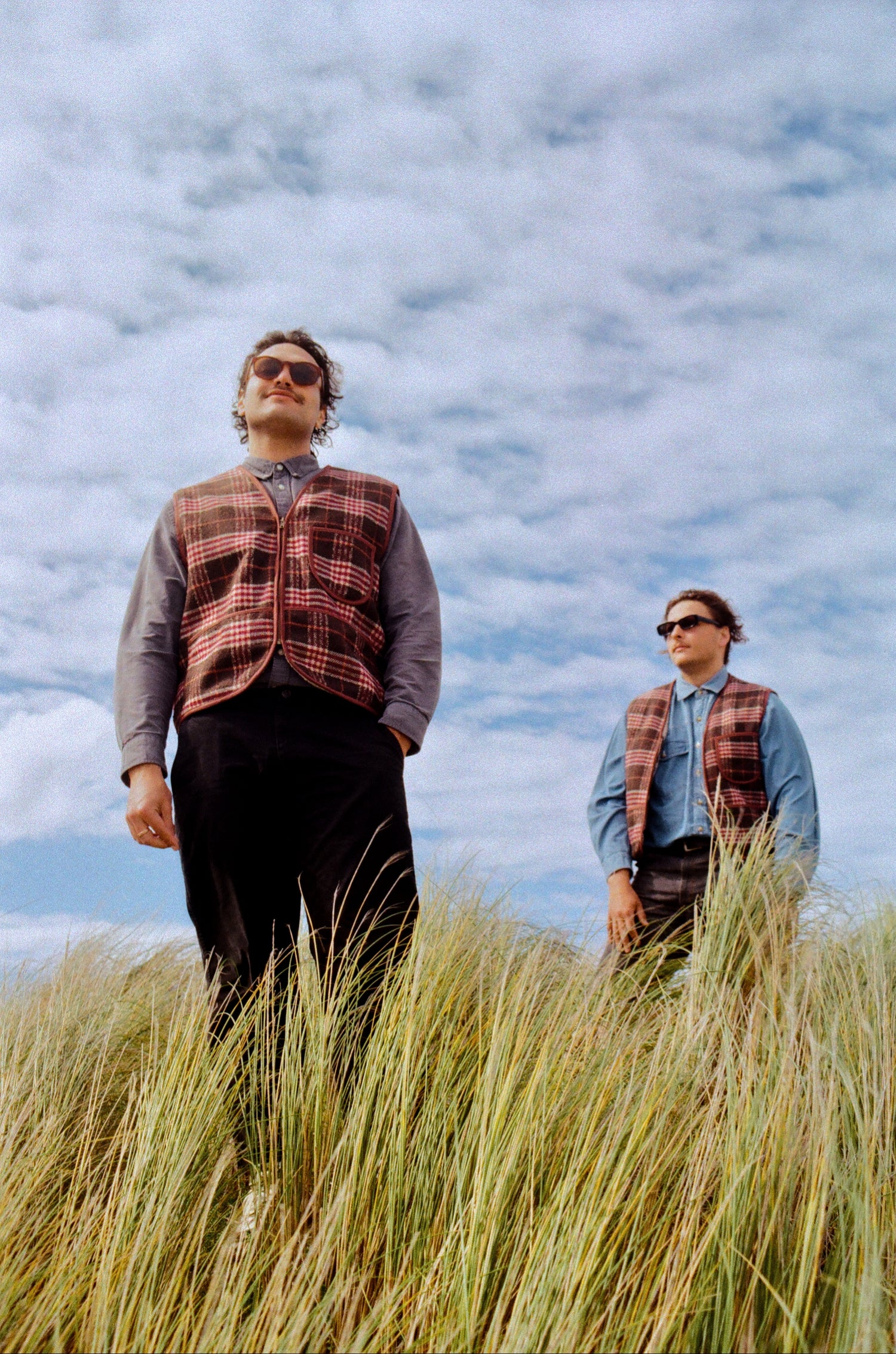 Two people standing in tall grass with a cloudy sky background