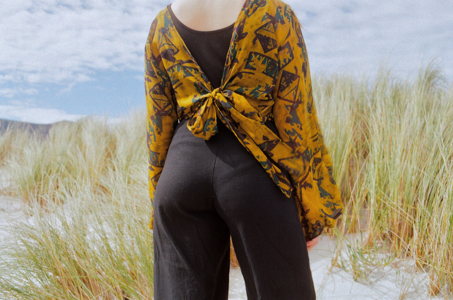 Person wearing a yellow patterned shawl over a dark outfit in the tall grass