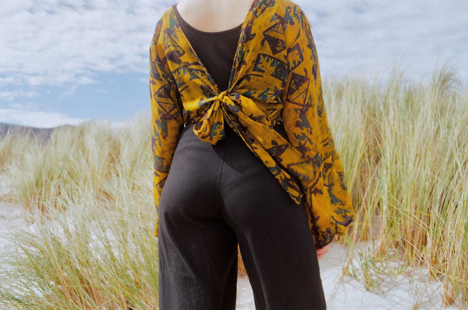 Person wearing a yellow patterned shawl over a dark outfit in the tall grass