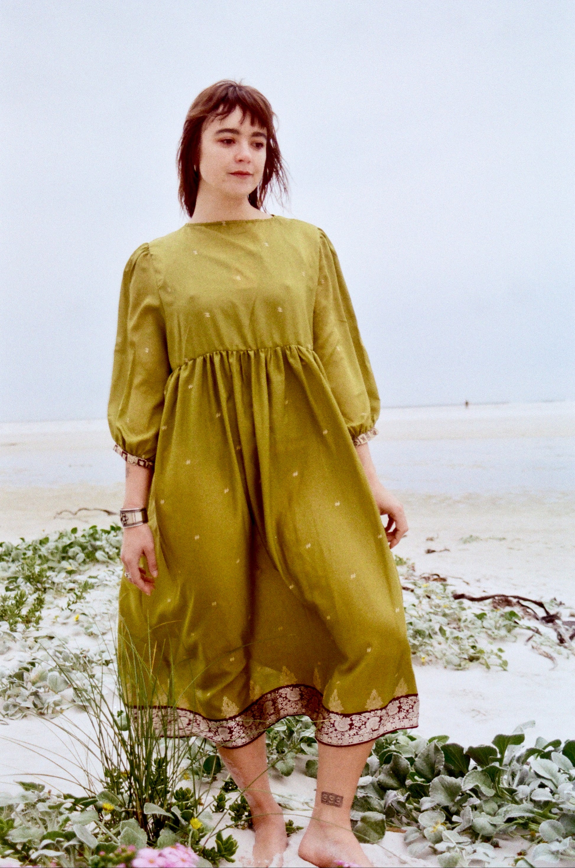 Woman in a green dress standing on a beach with a blurred background